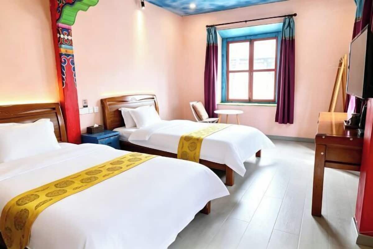 Ein Hotelzimmer mit zwei Betten, einem kleinen Tisch, einem Sessel, einem Fernseher und einem Fenster mit Vorhängen.