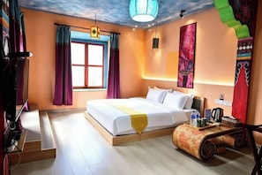 Una habitación de hotel con cama, escritorio, silla, ventana con cortinas y un cuadro en la pared.