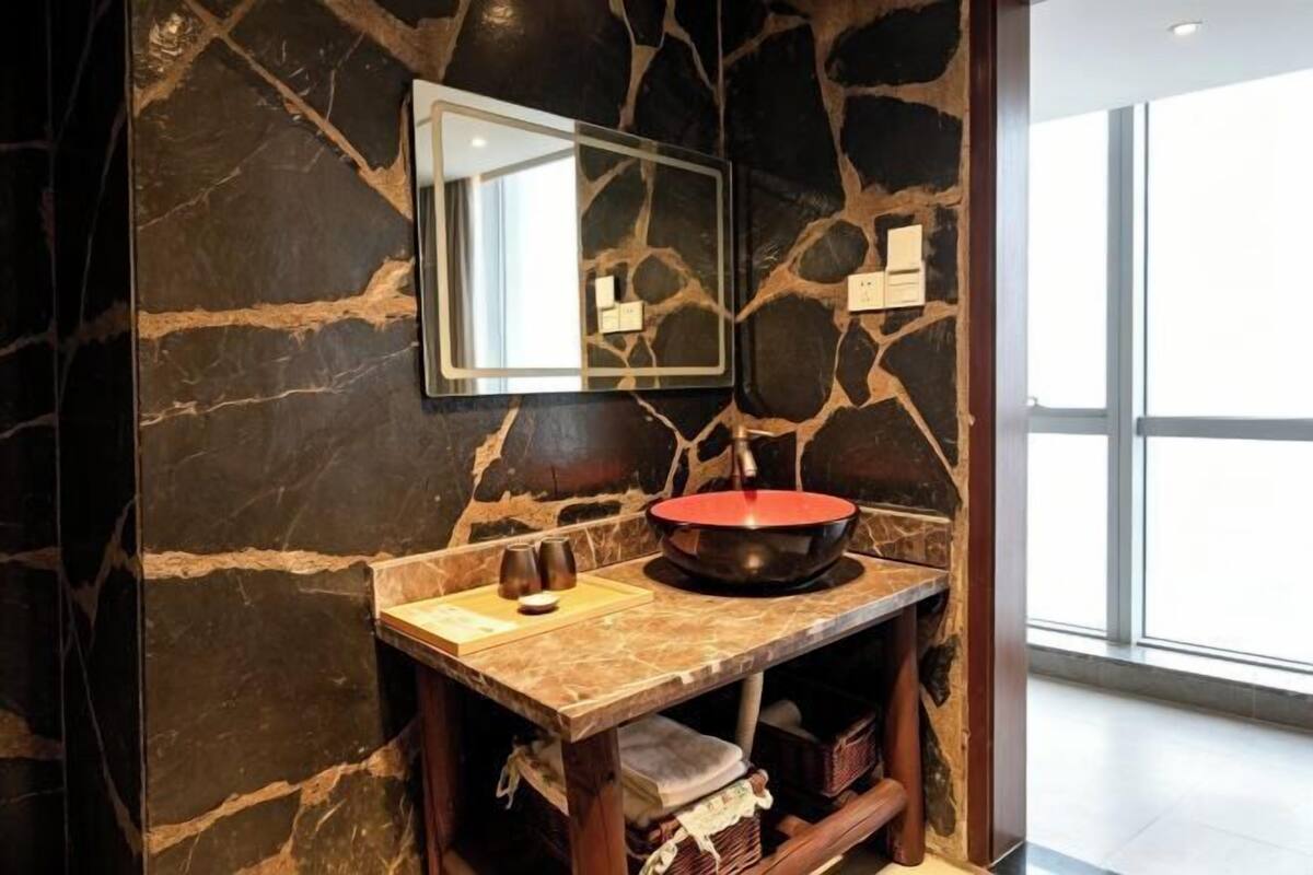 Ein Badezimmer mit Steinwand, Spiegel, Waschbecken mit roter Schüssel und Holz-Waschtisch.