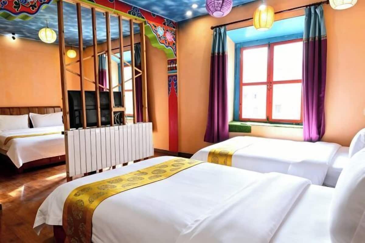 Ein Hotelzimmer mit zwei Betten, einem Fenster mit Vorhängen, einem Heizkörper und einem farbenfrohen Deckendesign.
