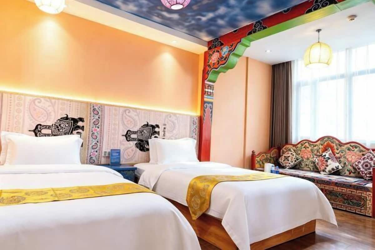 Ein Hotelzimmer mit zwei Betten, einer Wanddekoration, einer farbenfrohen Decke und einem Vorhangfenster.
