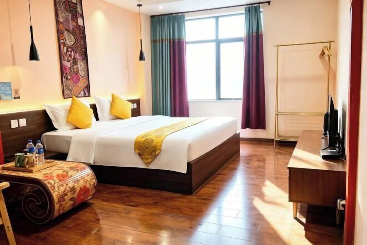 Ein Hotelzimmer mit Bett, Nachttisch, Schreibtisch, Stuhl, einem Fenster mit Vorhängen und einem Wandbild.