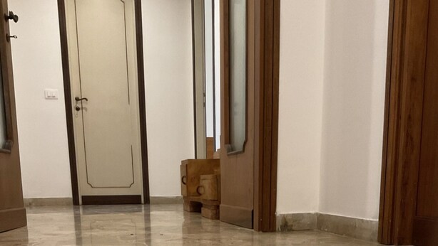 A hallway with a marble floor, wooden doors, and a small wooden cabinet.