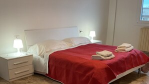 A bedroom with a bed, nightstands, a red bedspread, and a marble floor.