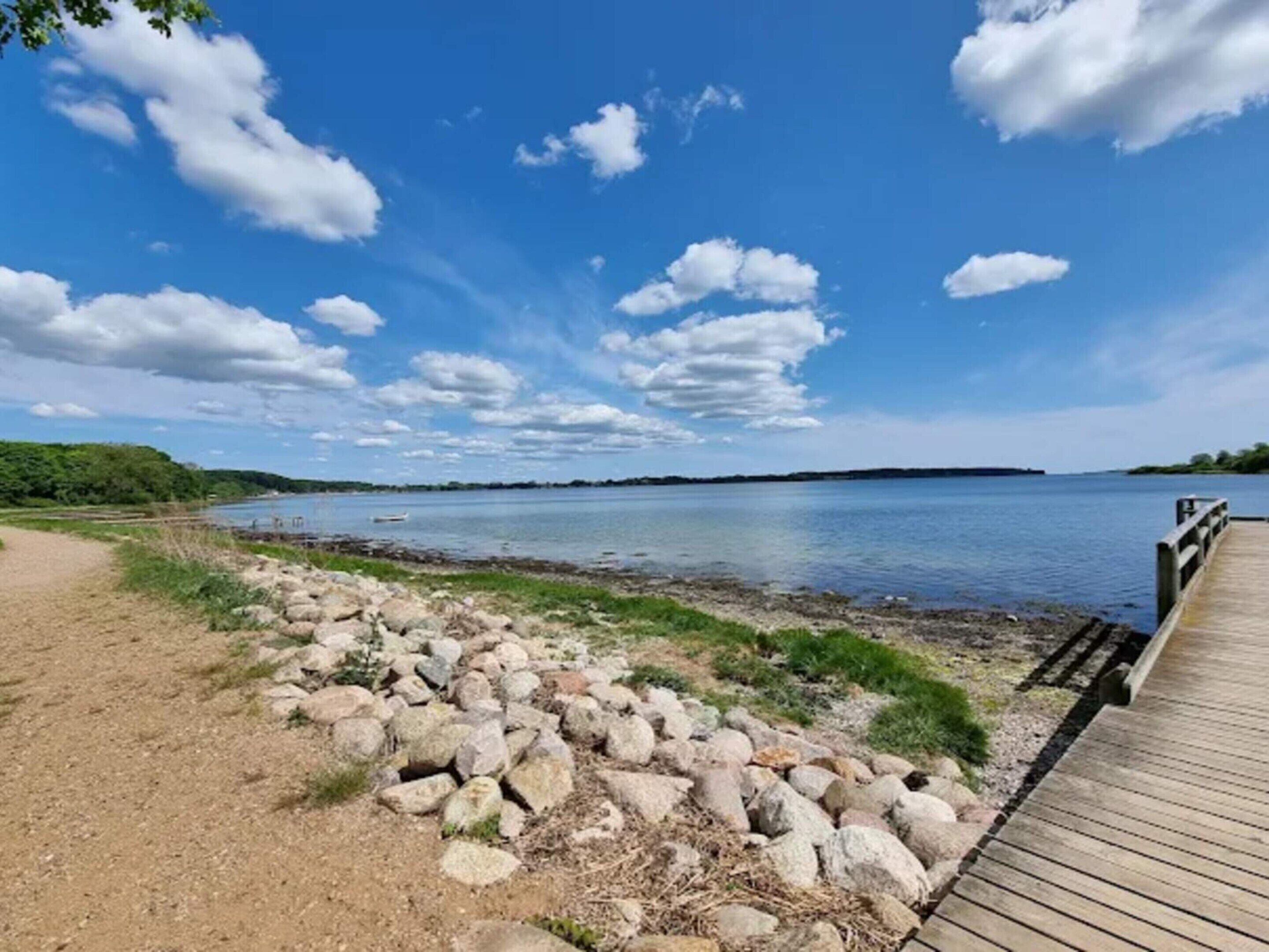 A wooden pier extending into a calm lake with a clear sky and scattered clouds.