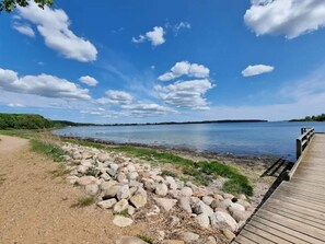 Une jetée en bois s’étendant dans un lac paisible, sous un ciel dégagé parsemé de quelques nuages.