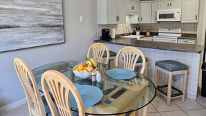 A modern kitchen with white cabinets, a microwave, and a stove. There is a glass dining table with chairs and a bowl of fruit.