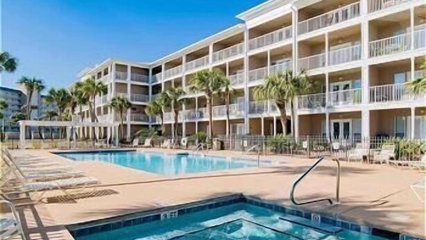 A hotel with multiple balconies, a swimming pool, and palm trees.