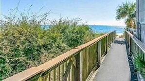 A narrow pathway leading to a beach with a wooden railing and a view of the ocean.