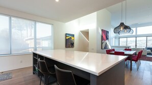 A modern kitchen with a large island, bar stools, and a dining area with red chairs. - NEW Construction, Magnificent NEW Townhome in dt Hood River w/Rivr views, garage (Hood River)
