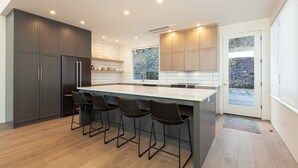 A modern kitchen with dark cabinets, a large island with bar stools, and a view through the window. - NEW Construction, Magnificent NEW Townhome in dt Hood River w/Rivr views, garage (Hood River)
