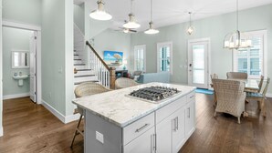 A spacious kitchen with a central island, a dining area with wicker chairs, and a staircase leading to another level. - 30A Home: 3 King Suites, Bunk Room, Golf Cart & Bikes, Half Mile to Sand (Santa Rosa Beach)