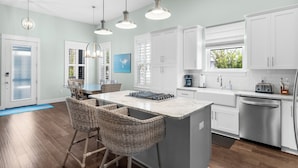 A modern kitchen with white cabinets, a central island with bar stools, stainless steel appliances, and pendant lighting. - 30A Home: 3 King Suites, Bunk Room, Golf Cart & Bikes, Half Mile to Sand (Santa Rosa Beach)