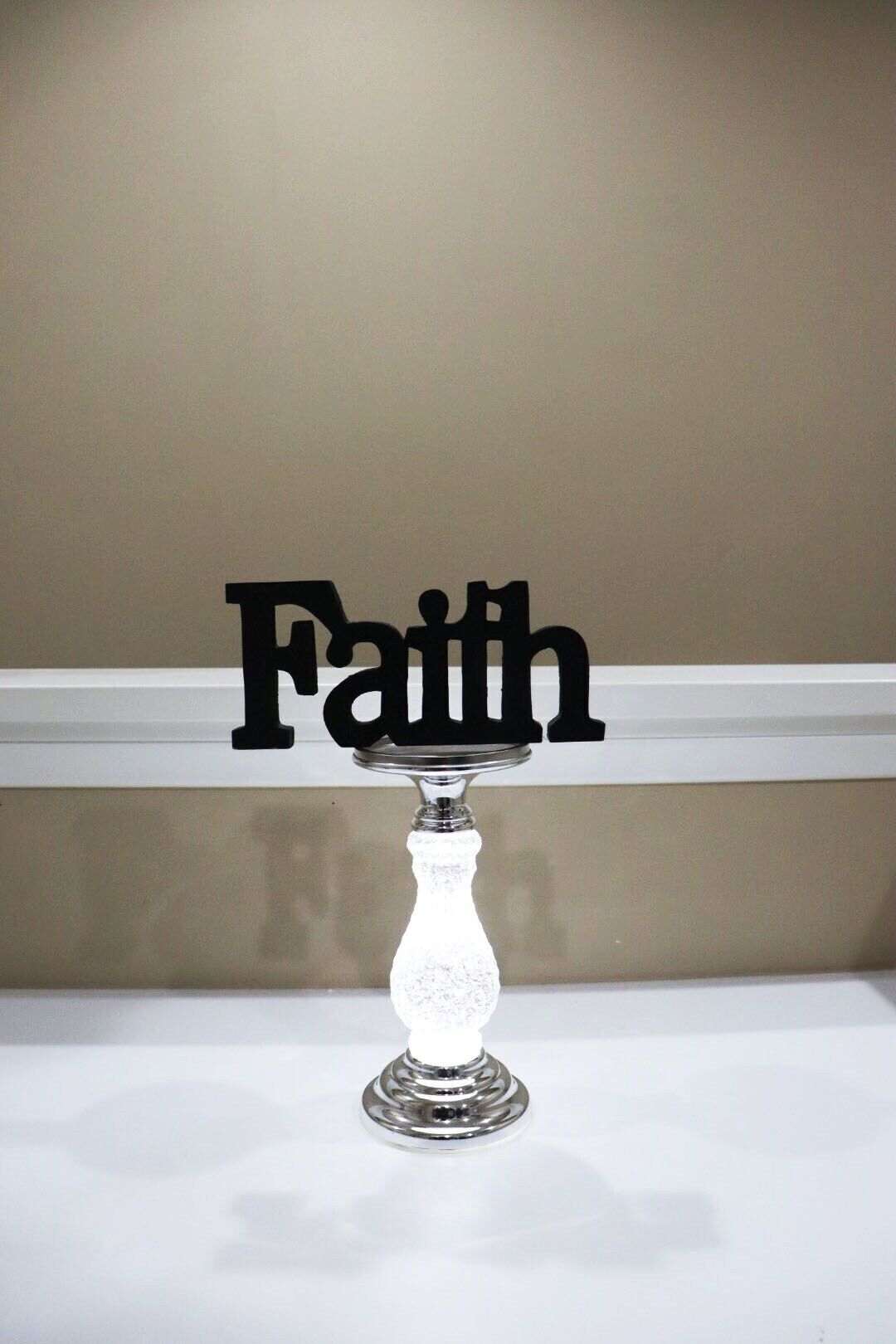 Une table en verre transparent, avec un pied en argent et une plaque noire sur le dessus portant l’inscription « Foi ».
