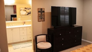A bedroom with a bed, a dresser, a chair, a television on the dresser, a mirror, and a bathroom visible in the background. - Pretty Relaxed Me: Pool, Spa, Clubhouse (Brea)