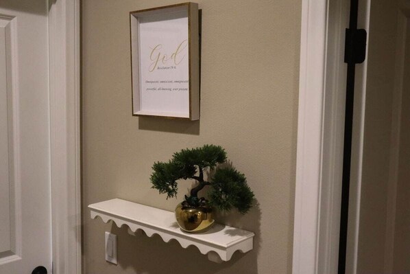 A framed inspirational quote on a wall, a small potted bonsai tree on a white shelf, and a door with a black handle.