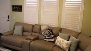 A living room with a beige sectional sofa, three white shutters, and a framed sign on the wall. - Pretty Relaxed Me: Pool, Spa, Clubhouse (Brea)