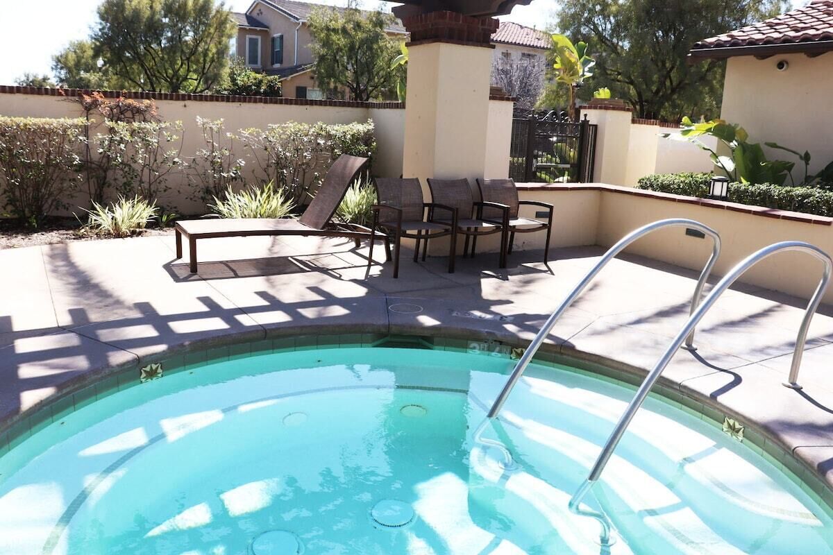 A swimming pool with a sun lounger and chairs, surrounded by a tiled deck and a low wall with plants.