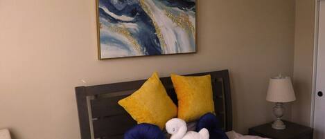 A bedroom with a bed, two pillows, a nightstand with a lamp, and a painting on the wall.
