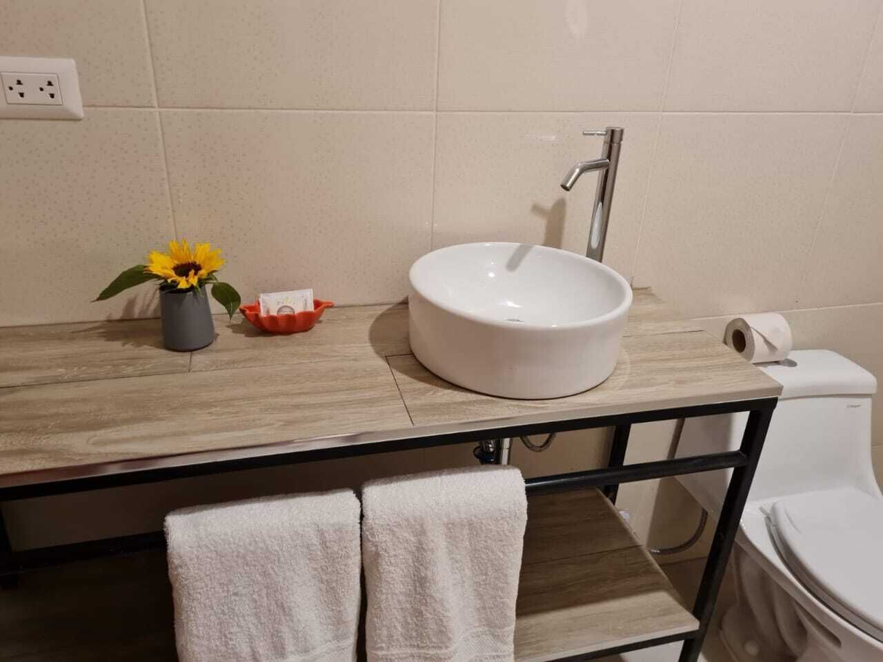 Une salle de bain avec un meuble-lavabo en bois, un lavabo blanc, des toilettes et un petit vase contenant un tournesol.