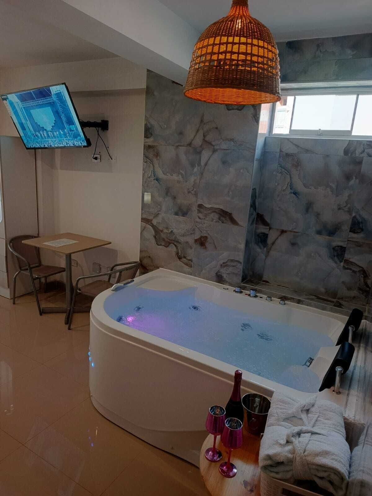 A modern bathroom with a freestanding bathtub, a flat-screen TV mounted on the wall, and a stone-textured wall.