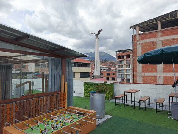 An outdoor patio area with a foosball table, seating, and a view of a cityscape with a tall monument.