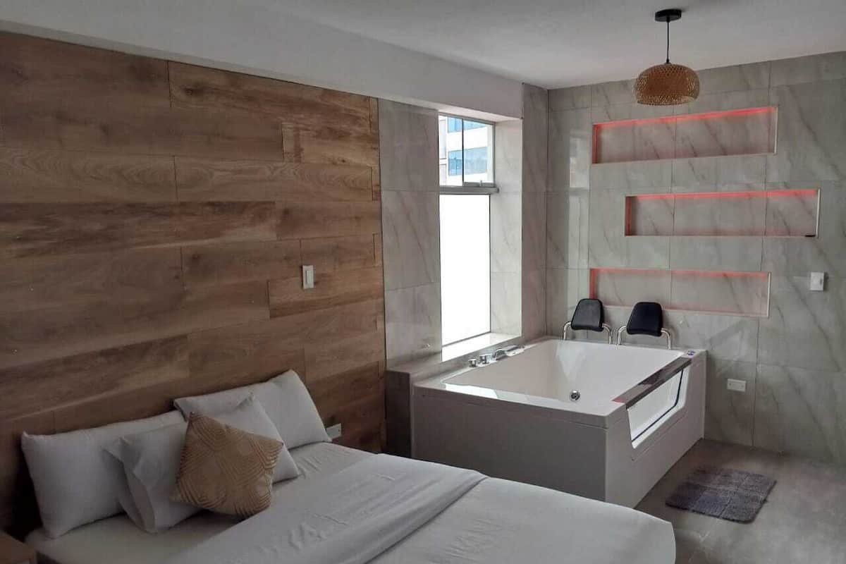 A modern bedroom with a large bed, a bathtub, and a wooden wall.