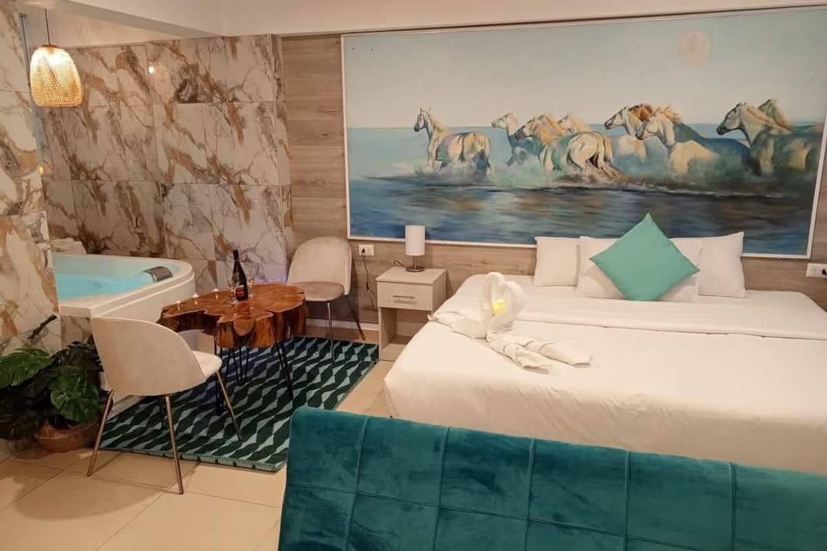 A modern hotel room with a large bed, a desk, a chair, a small table, and a painting of horses on the wall.