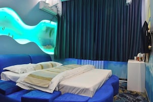 A room with a blue sofa, a bed with white bedding, a wall-mounted massage chair, and a curtain-covered window.