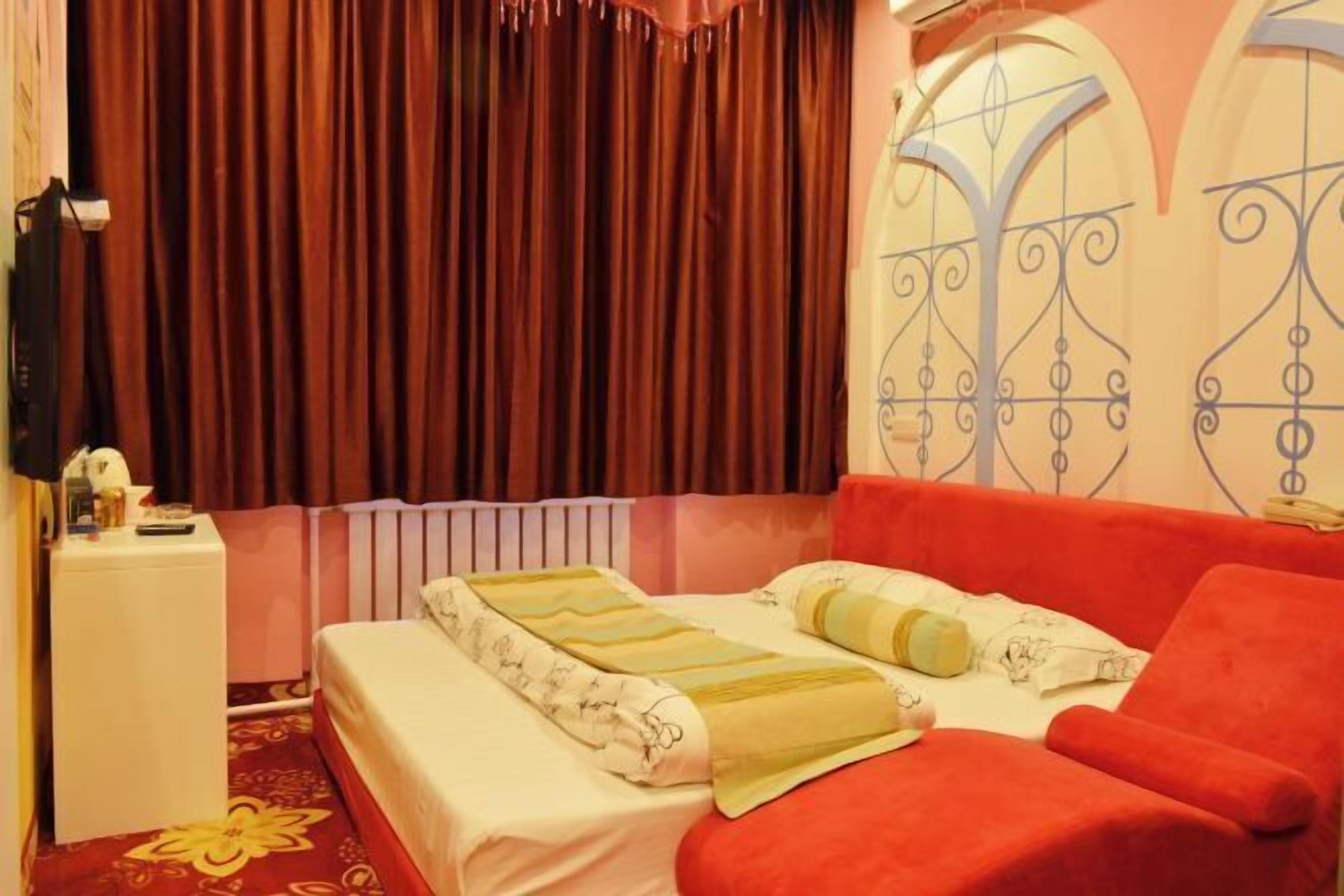 Una camera d'albergo con un letto, un divano rosso, un comodino bianco e una tenda.