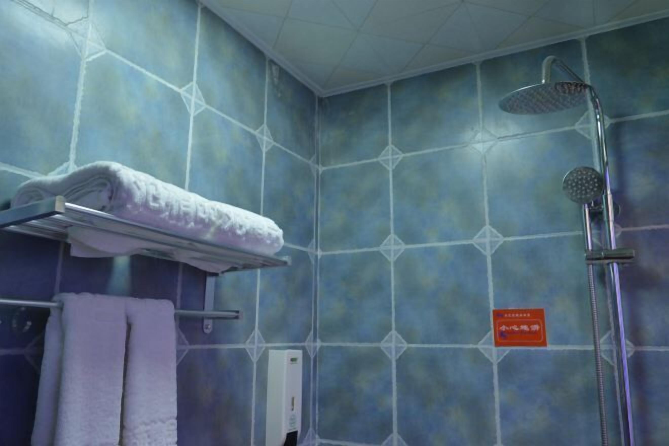 Ein Badezimmer mit blauen Fliesen, einem weißen Handtuch auf einem Halter, einer Duschbrause und einem Schild an der Wand.