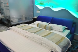 A hotel room with a bed, a nightstand, a lamp, and a wall-mounted aquarium.