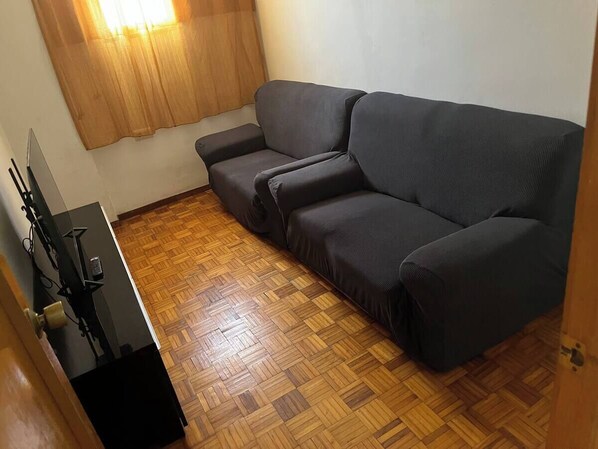 A room with a dark grey sofa, a wooden herringbone floor, and a small black table with electronic devices.