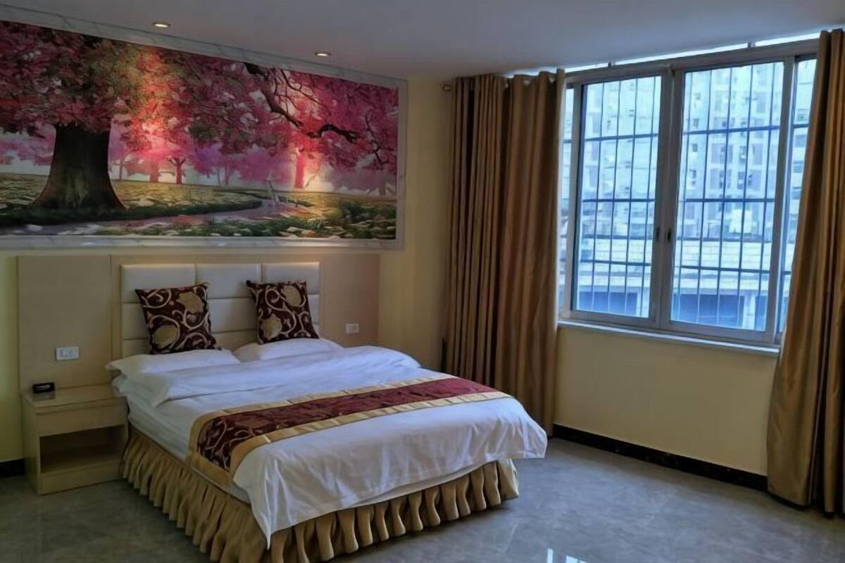 Habitación de hotel con una cama grande, una mesita de noche, un cuadro en la pared y una ventana con cortinas.