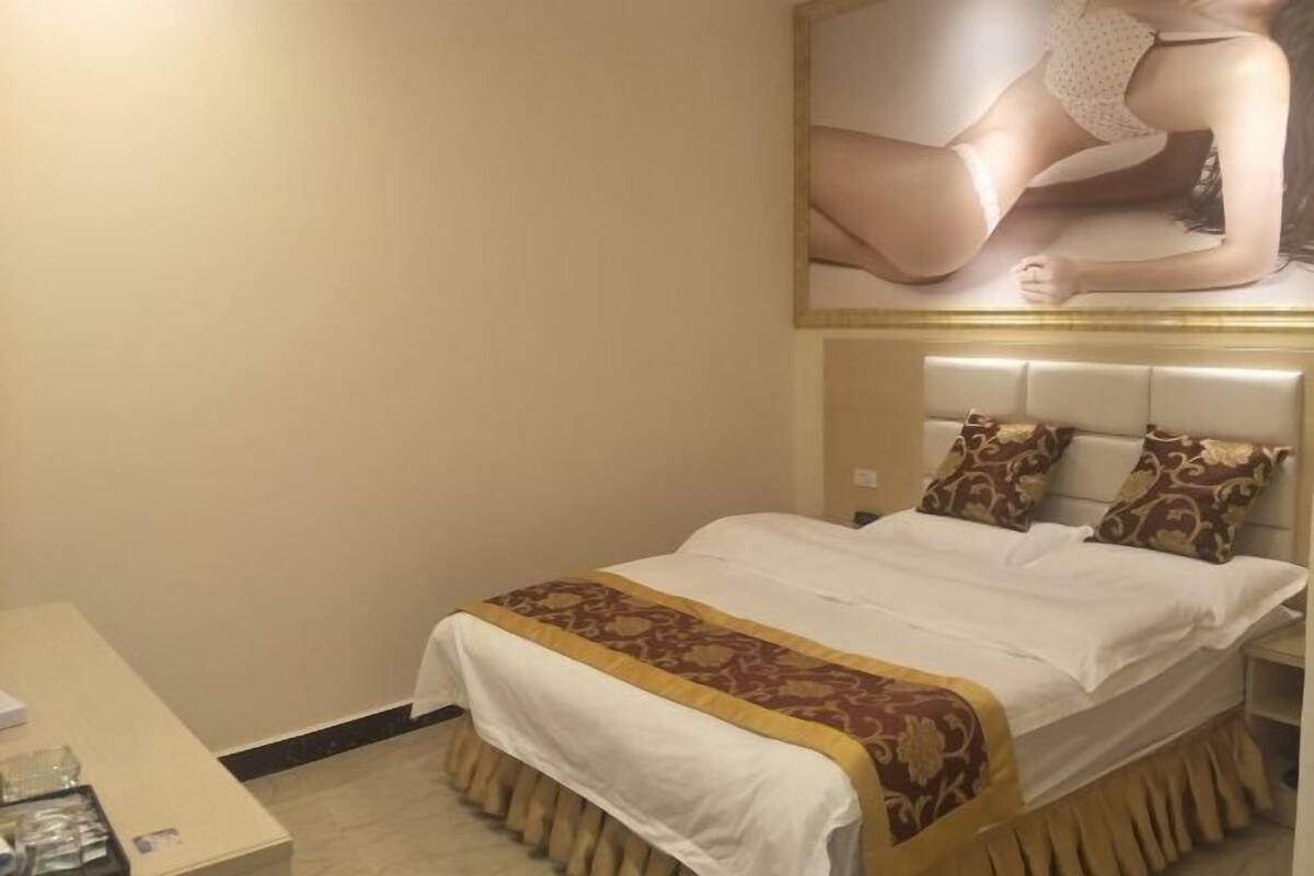 Una habitación de hotel con cama, mesita de noche, escritorio con silla y un cuadro en la pared.