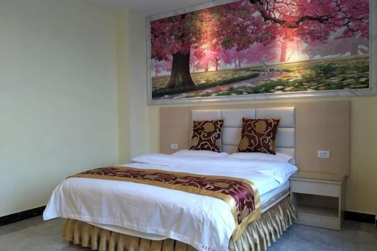Une chambre à coucher avec un lit, des oreillers, une tête de lit et un tableau représentant un arbre.