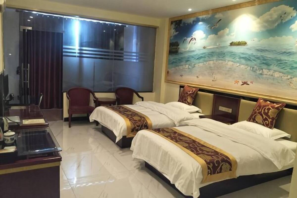 Habitación de hotel con dos camas, un escritorio, una silla y un cuadro grande de una playa.
