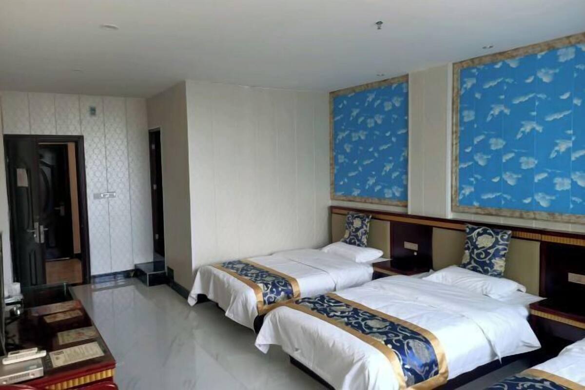 Habitación de hotel con dos camas, cabecero de madera, un escritorio pequeño y una pared decorativa con estampado floral.