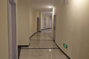 Um corredor comprido e estreito com chão de mármore e portas em ambos os lados.