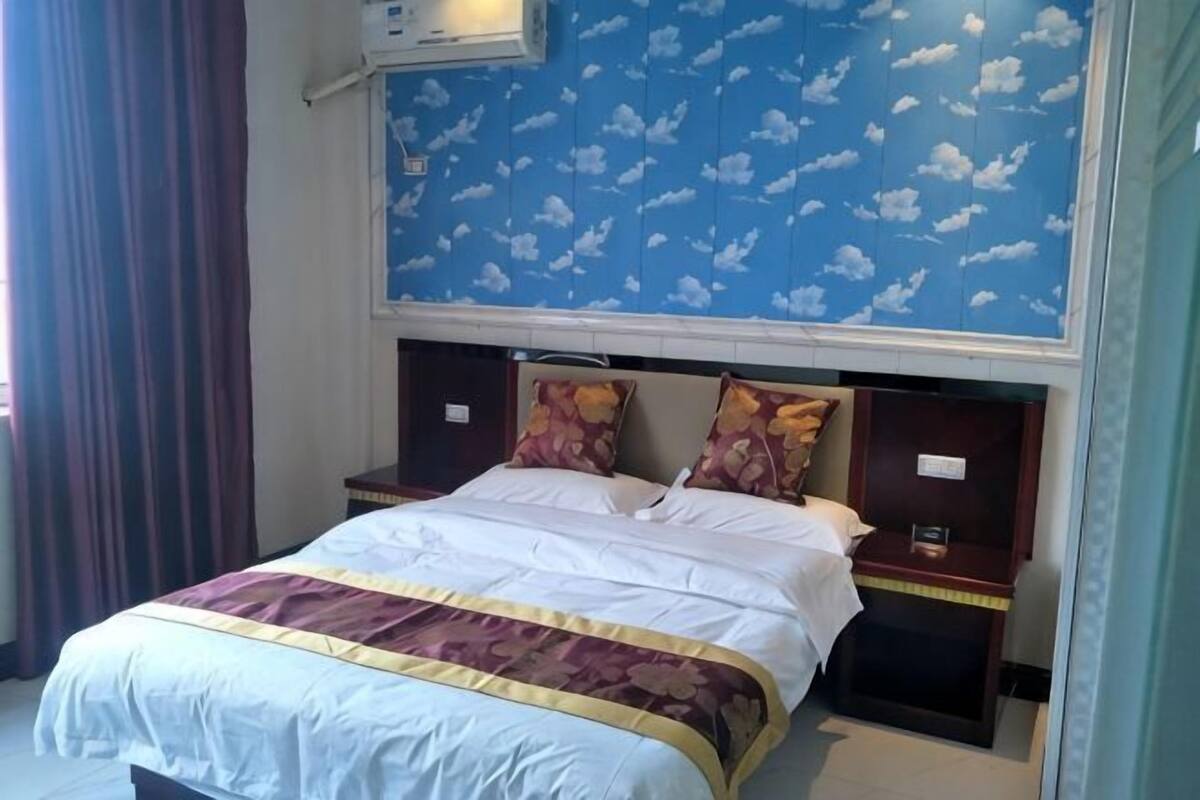 Una habitación de hotel con una cama, cabecera con estampado floral y una mesita de noche con lámpara.