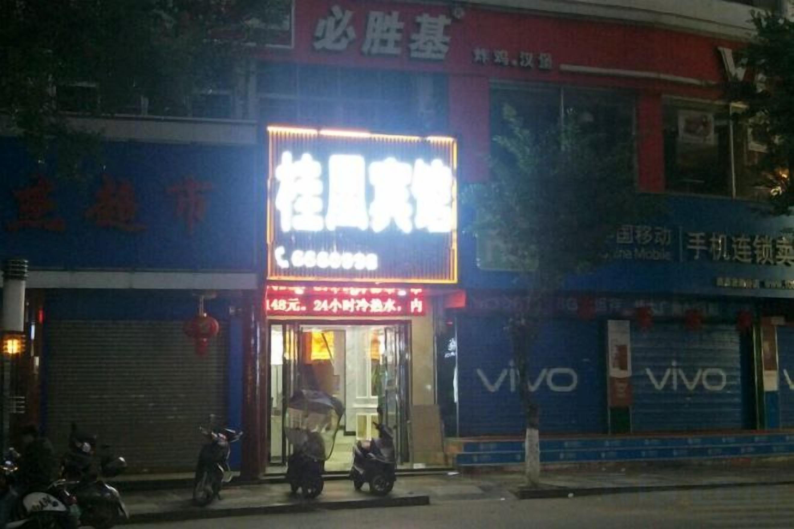 A storefront with a brightly lit sign, a closed shutter door, and a scooter parked outside.