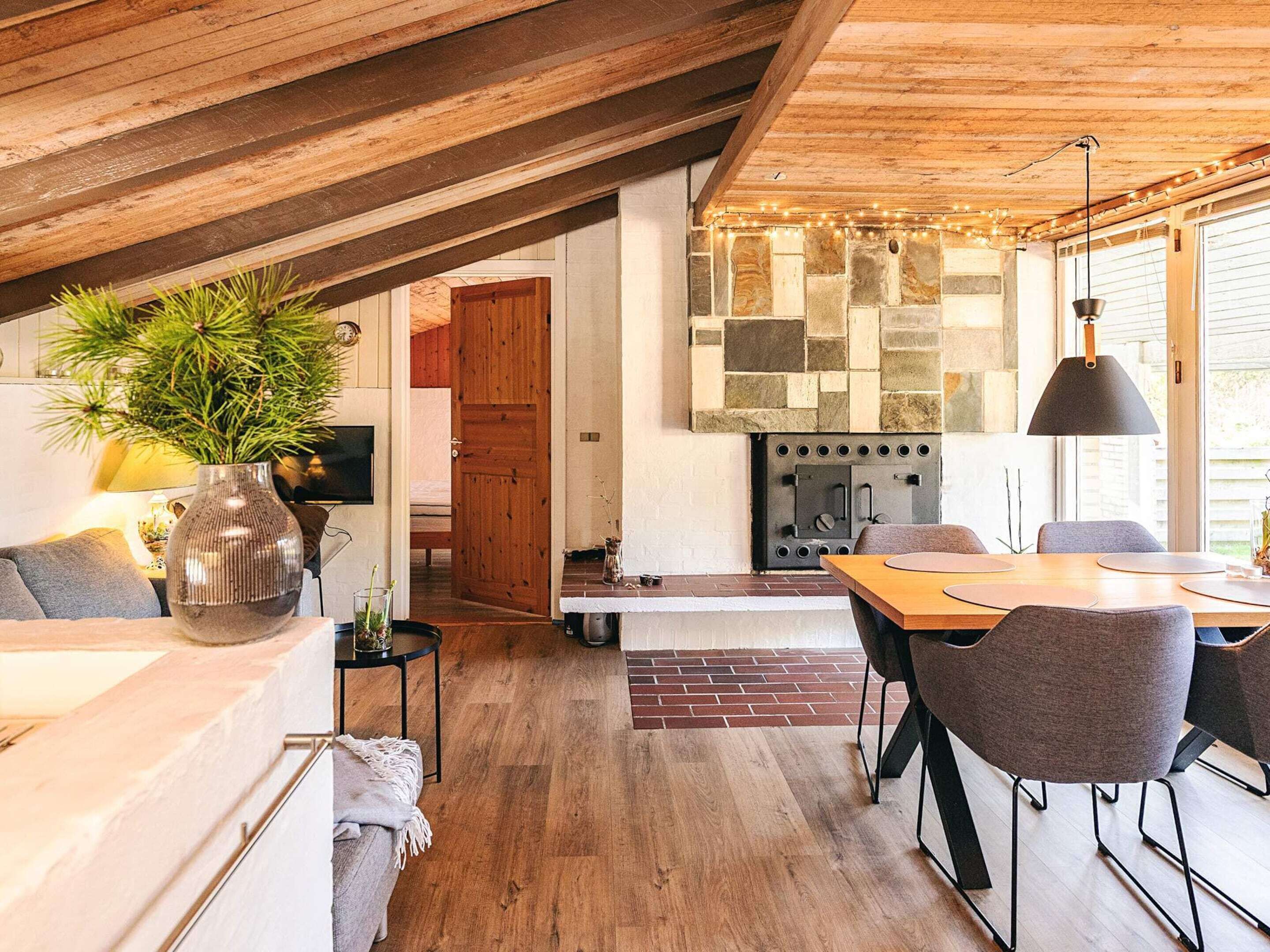 Una sala de estar acogedora con chimenea, vigas de madera en el techo y una mesa de comedor con sillas.