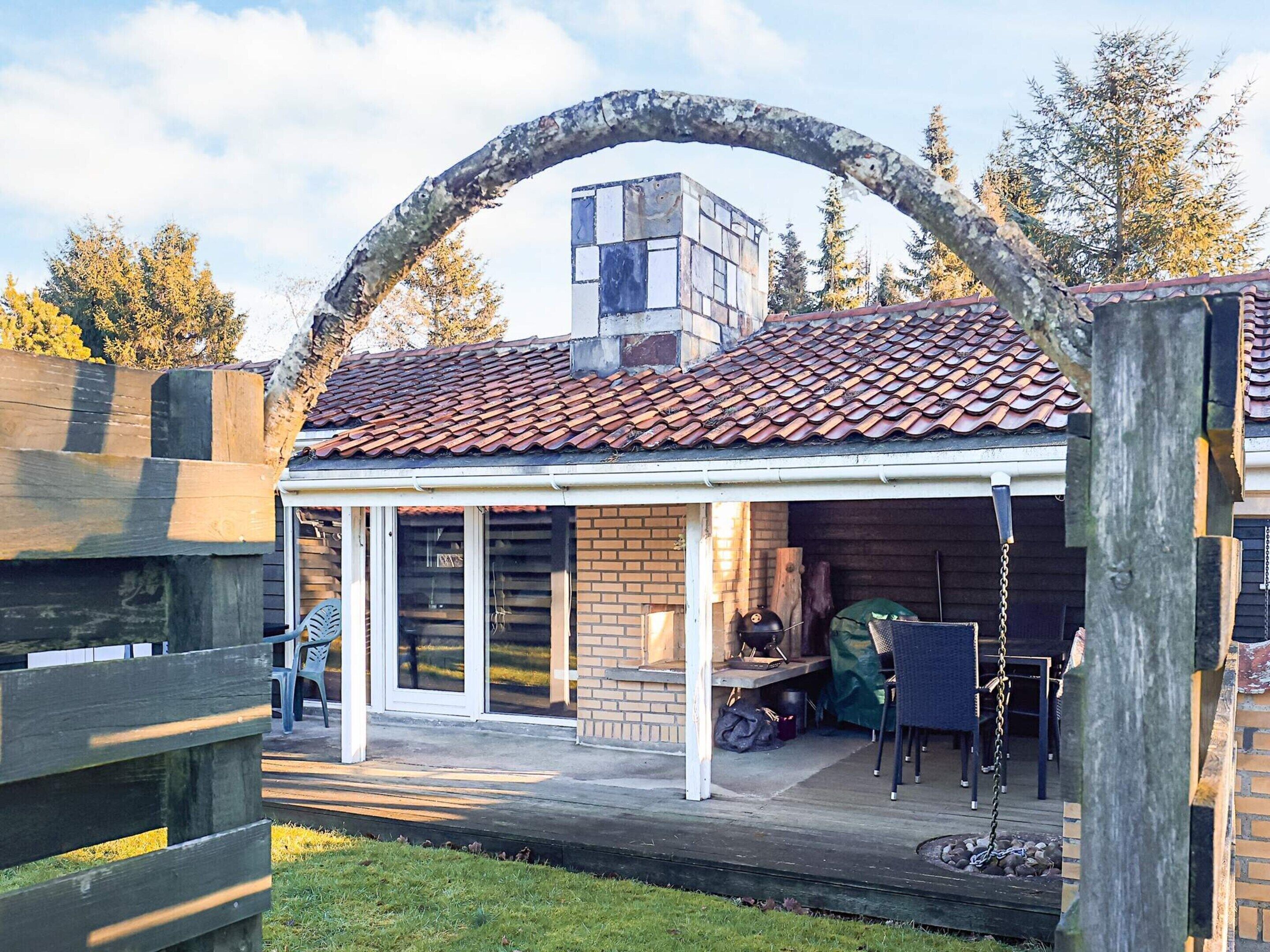 A covered outdoor area with a brick wall, a wooden deck, and a metal grill.