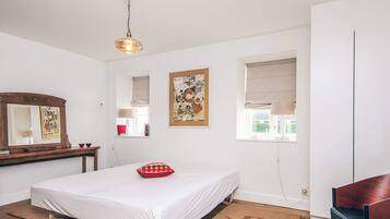 Un dormitorio con cama, cómoda de madera, espejo, ventana con persianas y lámpara colgante.