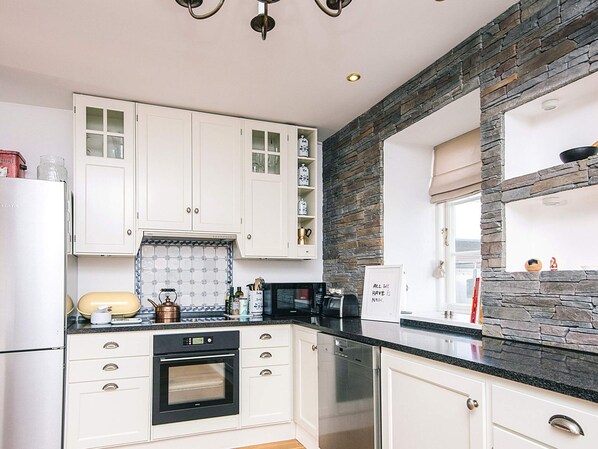 A modern kitchen with white cabinets, a black countertop, a built-in oven, and a dishwasher.