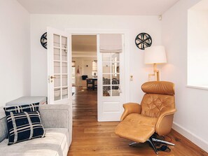 A room with a leather recliner, a grey sofa with patterned cushions, and a white door leading to another room.