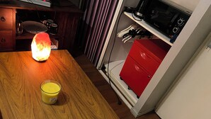Ein Holztisch mit einer brennenden Kerze und einem Glaslaternenfuß. Im Hintergrund ist ein roter Schrank mit einer Mikrowelle zu sehen.
