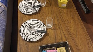 Ein Holztisch mit zwei weißen Tellern, Besteck, einem Glas, einer Kerze und einem Korb mit Snacks.