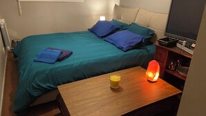 Ein Schlafzimmer mit Bett, Kissen, Nachttisch mit Lampe, Fernseher und Heizung.