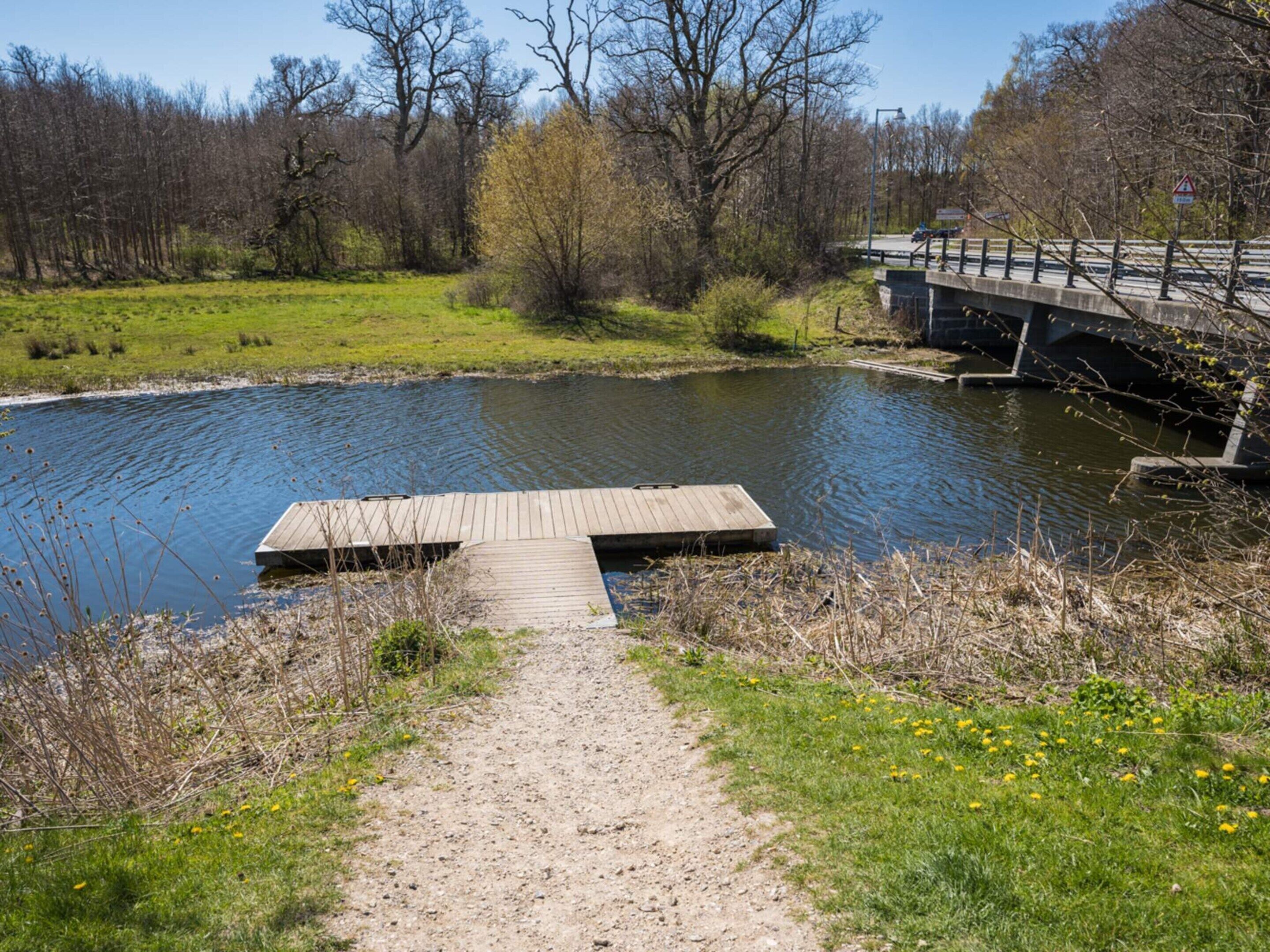 Une rivière avec un quai en bois, un pont et un sentier menant à l’eau.